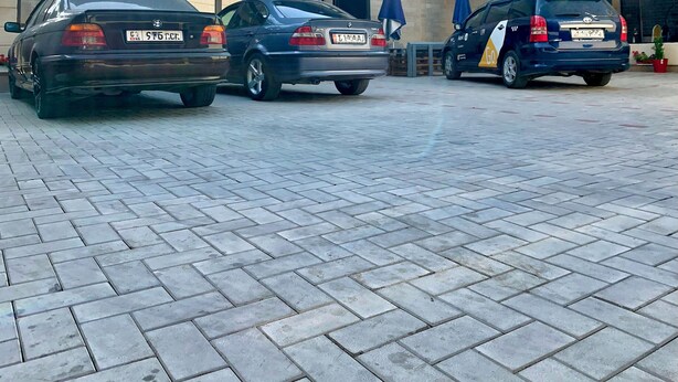 A parking area with three cars, a building with a tiled roof, and a clear sky. - Nomad - Hostel (Bishkek)