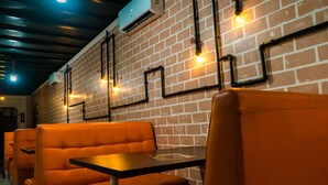 A restaurant interior with brick walls, orange cushioned seating, and exposed ductwork. - Nomad - Hostel (Bishkek)