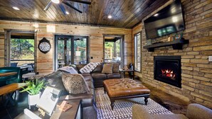 Un salón acogedor con chimenea, muebles de cuero y un televisor grande montado en una pared de piedra.