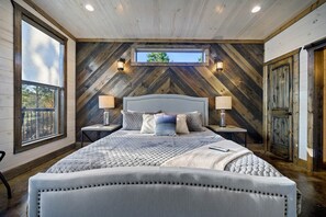 Une chambre à coucher avec un grand lit, deux tables de chevet avec des lampes, une fenêtre et un mur en bois avec un motif en chevrons.