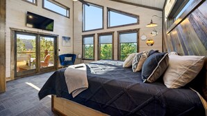 Un dormitorio con una cama grande, varias ventanas, un ventilador de techo y un televisor montado en la pared.