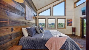 Un dormitorio amplio con una cama grande, varios ventanales, paredes de madera y un ventilador de techo.