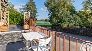 Eine Terrasse mit Tisch und Stühlen, Blick auf einen See und eine Steinmauer.