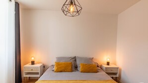 Ein Schlafzimmer mit einem Bett, zwei Nachttischen, einer geometrischen Lampe und einem Logo an der Wand.
