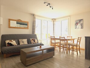 A living room with a grey sofa, wooden coffee table, and a dining area with wooden chairs and a table. - Beautiful apartment of 53m² located in the heart of the resort for 6/8 people (Les Deux Alpes)