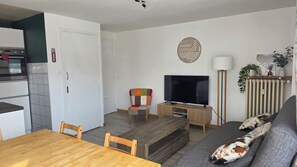 A modern living room with a wooden dining table, a colorful armchair, a flat-screen TV, a floor lamp, and a sofa with a dog. - Beautiful apartment of 53m² located in the heart of the resort for 6/8 people (Les Deux Alpes)