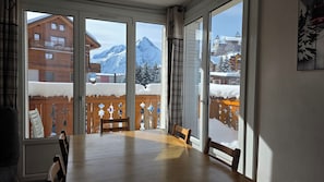 A dining area with a large table and chairs, a wooden fence, and a view of snow-covered mountains and buildings. - Beautiful apartment of 53m² located in the heart of the resort for 6/8 people (Les Deux Alpes)