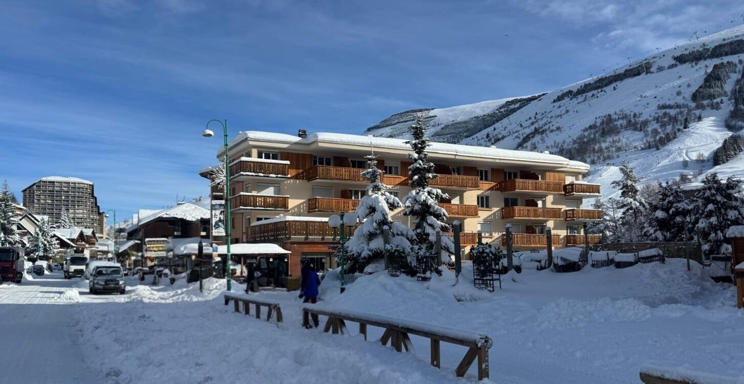 Un hôtel à plusieurs étages doté de balcons, entouré d’arbres couverts de neige et avec une chaîne de montagnes en toile de fond.