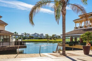 A waterfront property with a pool, palm trees, and a view of a golf course.