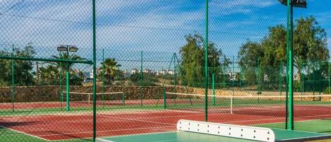 A tennis court with a green net, a table tennis table, and a fence.