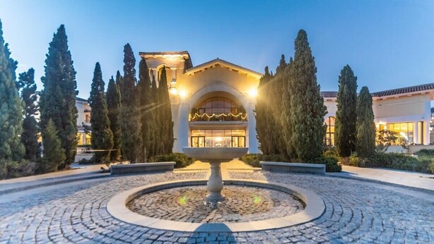 A courtyard with a central fountain, surrounded by cobblestone pavement and tall cypress trees.