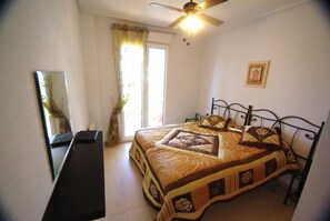 A bedroom with a bed, a ceiling fan, a window with curtains, and a wall-mounted mirror.