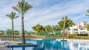 A swimming pool with palm trees, a fence, and a building in the background.