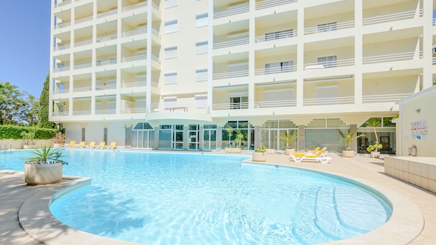 Ett modernt hotell med en swimmingpool, flera balkonger och ett välskött trädgårdsområde.