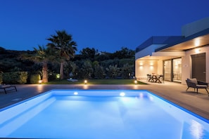 A modern outdoor pool area with a patio, seating, and a well-lit building.