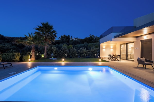 A modern outdoor pool area with a patio, seating, and a well-lit building.