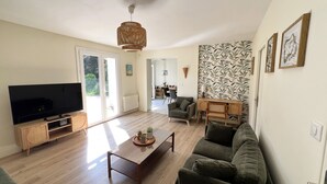 A living room with a TV, sofa, coffee table, and a dining area with chairs and a table. - LocaJard House "Les Conches" between sea and forest, 100 m², 3 bedrooms (Jard-sur-Mer)