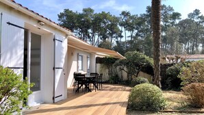 A wooden deck with a table and chairs, surrounded by greenery and trees. - LocaJard House "Les Conches" between sea and forest, 100 m², 3 bedrooms (Jard-sur-Mer)