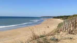 A sandy beach with gentle waves, a wooden fence, and sparse vegetation. - LocaJard House "Les Conches" between sea and forest, 100 m², 3 bedrooms (Jard-sur-Mer)