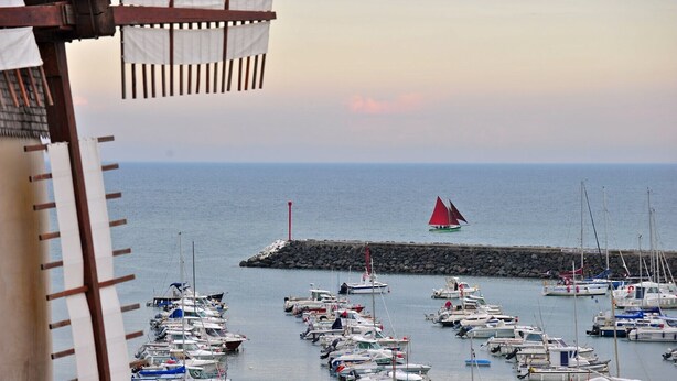 A marina with numerous boats docked, a pier with a red pole, and a sailboat with red sails in the distance. - LocaJard House "Les Conches" between sea and forest, 100 m², 3 bedrooms (Jard-sur-Mer)