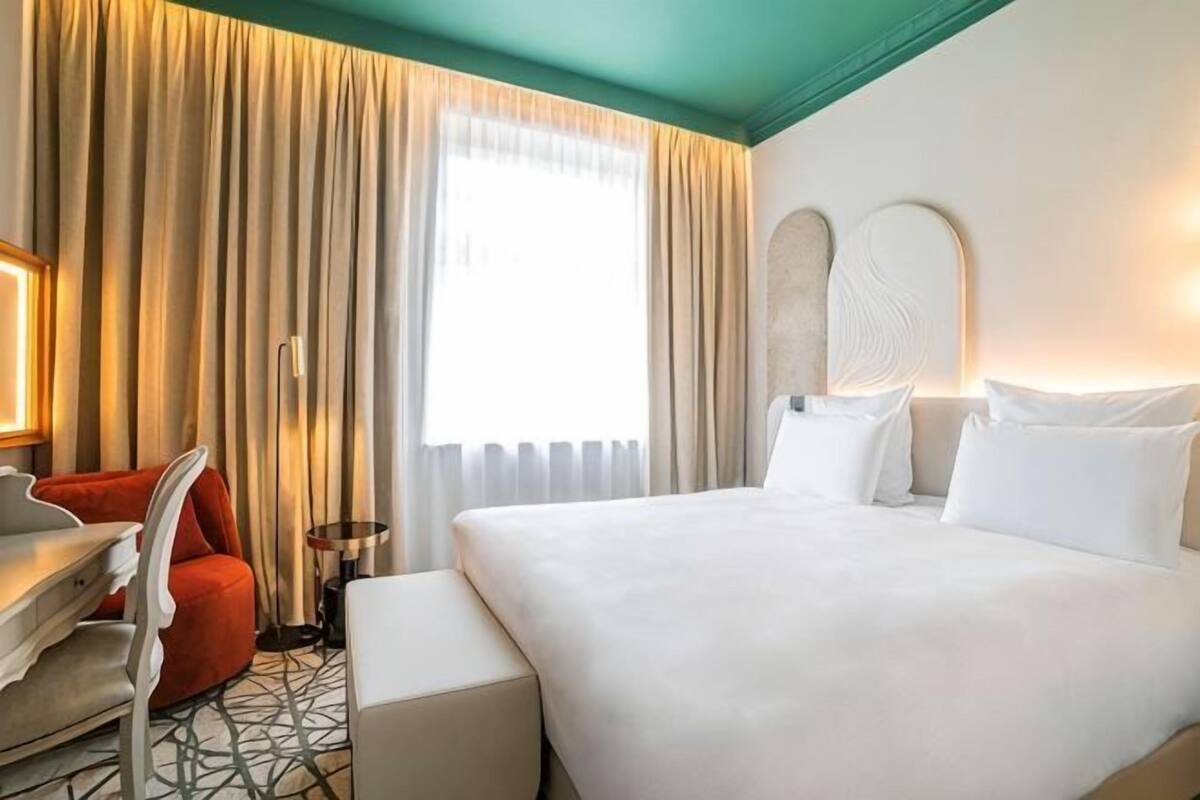 A hotel room with a bed, a desk, a chair, and a window with curtains.