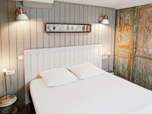 A room with a bed, two wall-mounted lamps, a wooden shelf with decorative items, and a rustic door. - L'appart de la Ferté - In the heart of Saint Valery's main street (Saint-Valery-sur-Somme)
