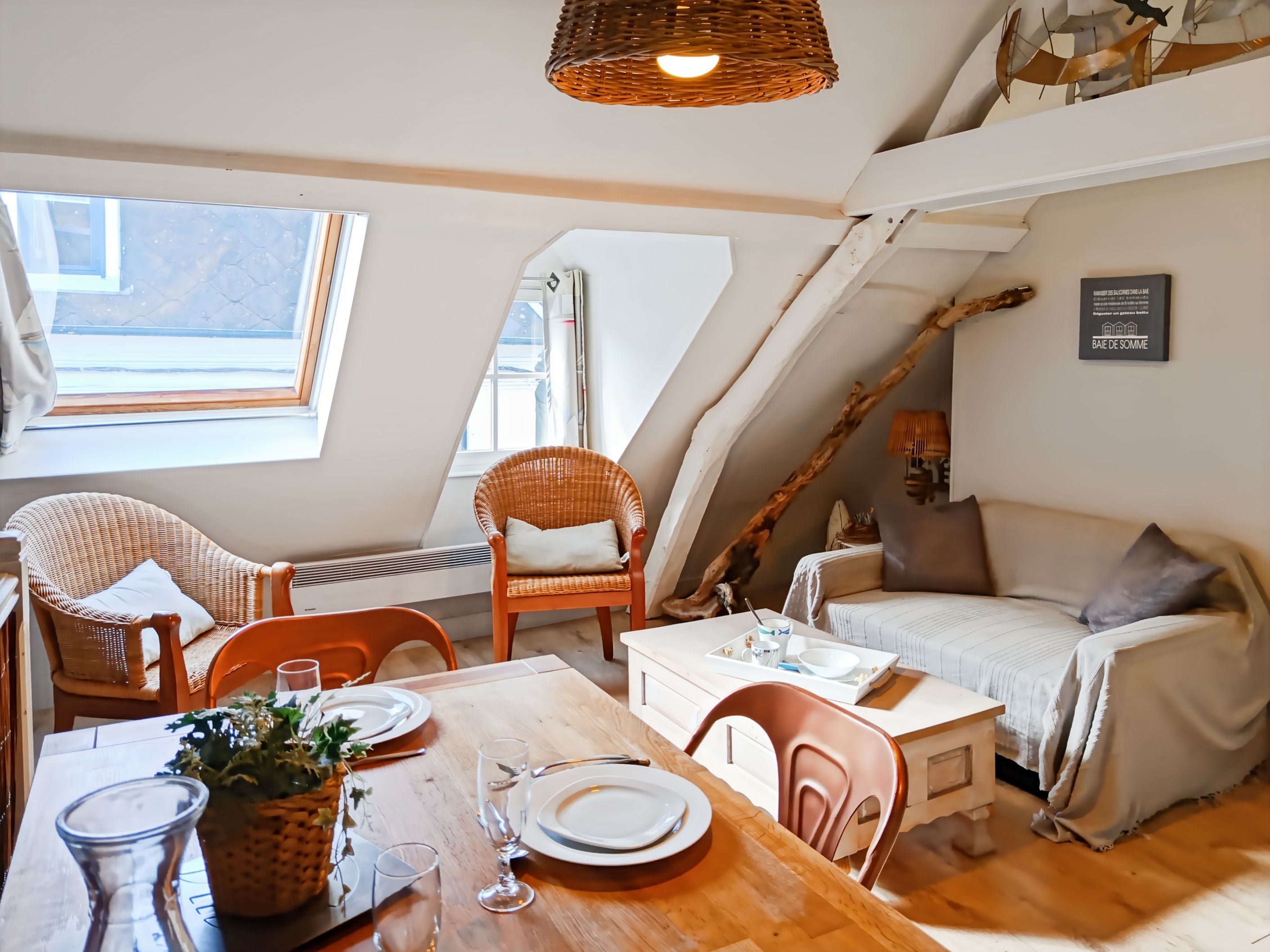 A cozy loft-style room with a dining table set for two, a sofa, and a large window providing natural light.