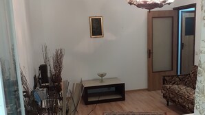 Un salón con suelo de madera, un tapiz estampado, un sofá, una mesa de comedor, una araña y una puerta con espejo.