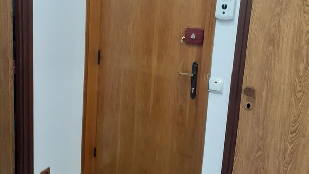 Una puerta de madera con un pequeño ventanal en la parte superior, un timbre y un letrero que indica una salida.