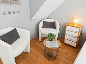 A modern living room with a white sofa, a smaller armchair, a wooden side table with a plant, and a wooden cabinet with drawers. - Le studio de la Ferté - In the heart of Saint Valery's main street (Saint-Valery-sur-Somme)