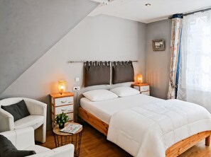A bedroom with a bed, two bedside tables, a nightstand, a chair, and a small table with a plant and a magazine. - Le studio de la Ferté - In the heart of Saint Valery's main street (Saint-Valery-sur-Somme)