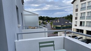 A balcony with a table and chair, overlooking a street with parked cars and residential buildings. - Very attractive, fully-furnished, luxury T2 apartment 5 minutes' walk from the center. (Divonne-les-Bains)