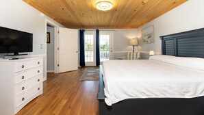 A bedroom with a wooden ceiling, a bed, a TV, a dresser, and a door leading to a balcony. - Saltwater Therapy - Ocracoke Island (Ocracoke)