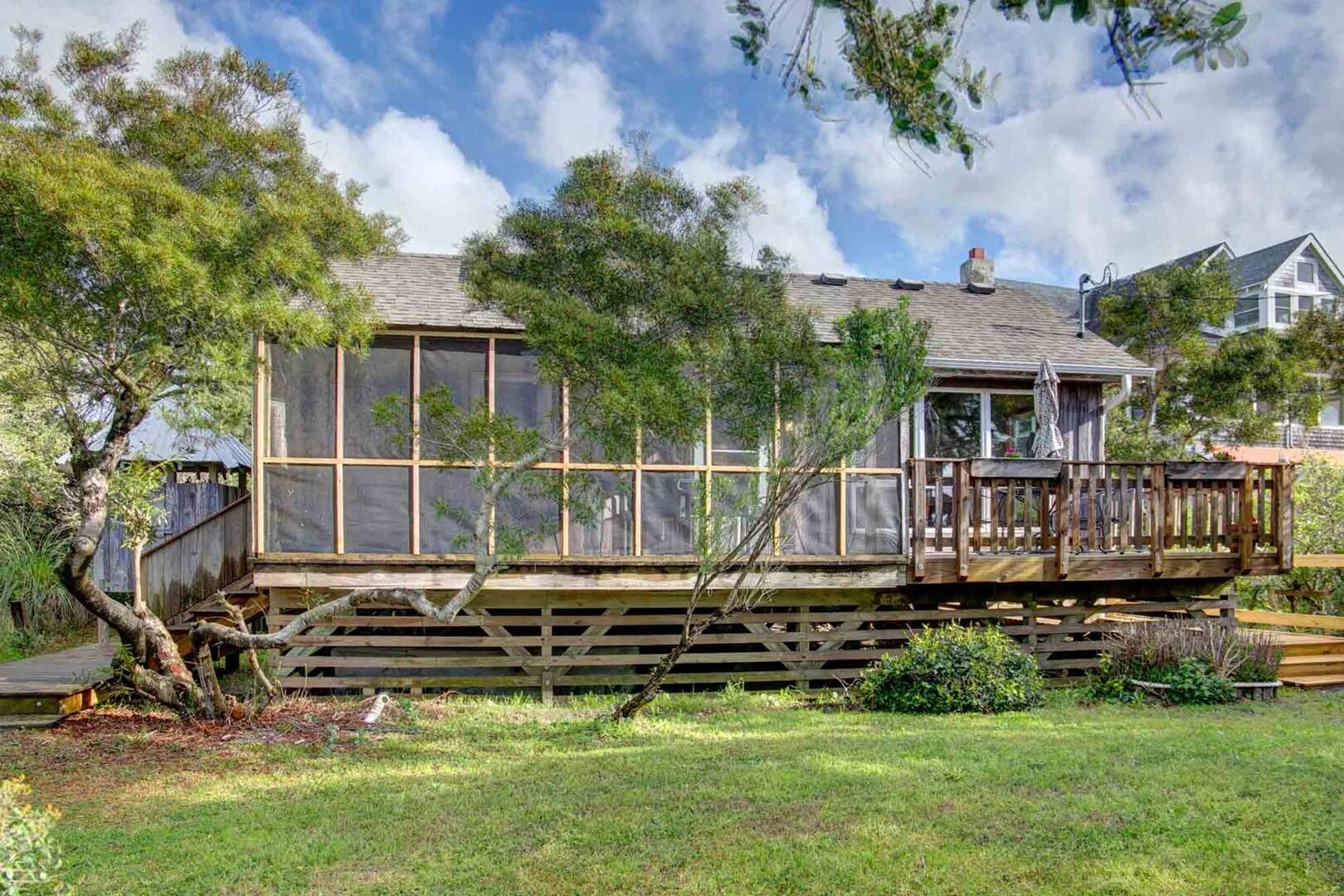 Een houten huis met terras, omgeven door bomen en een gazon.