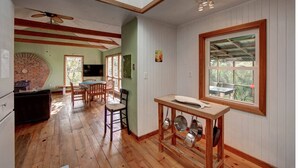 Eine gemütliche Küche mit Holzböden, einem Essbereich mit Tisch und Stühlen, einem Backofen aus Ziegelsteinen und einem großen Fenster mit Aussicht.