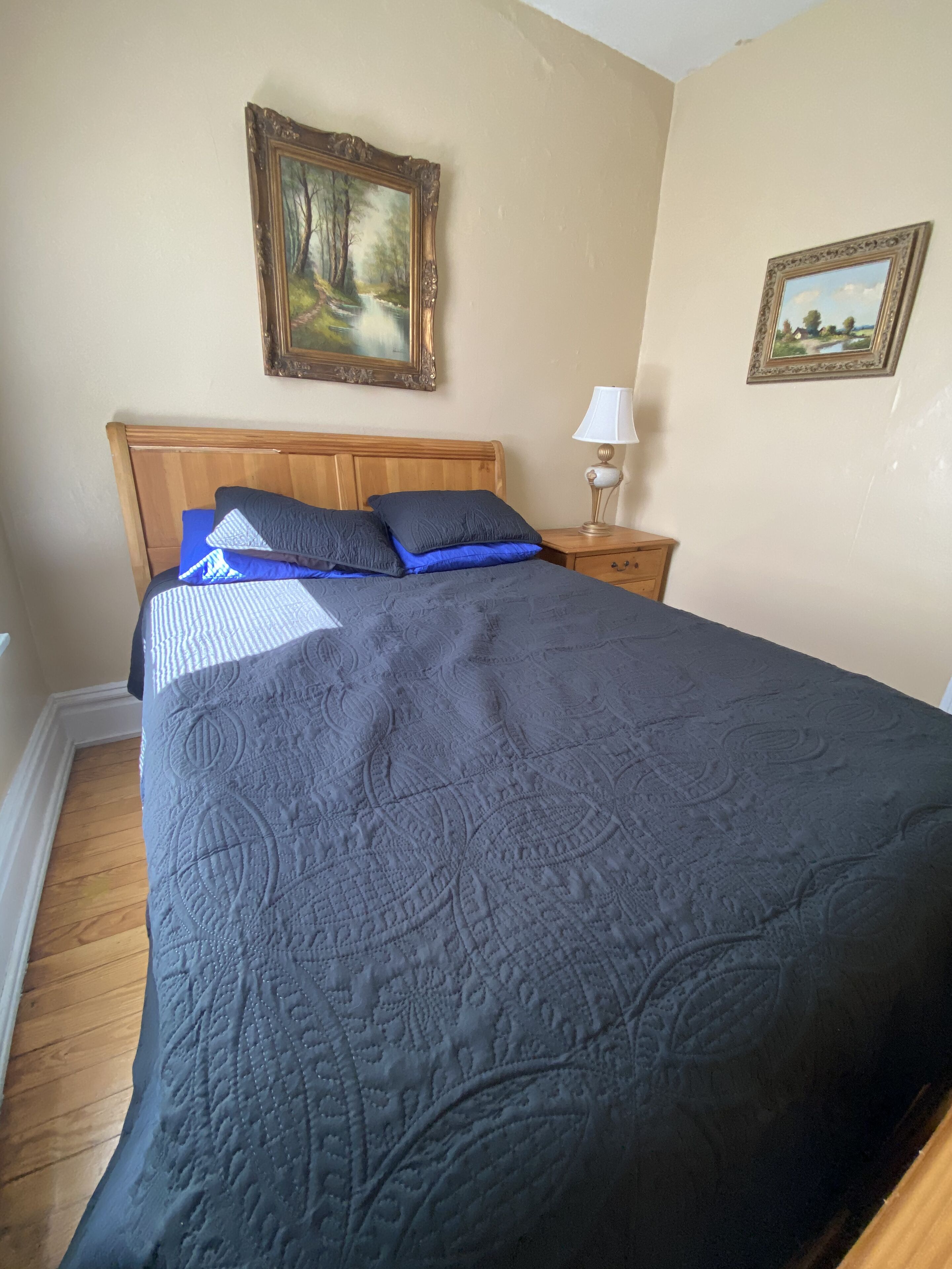 A bedroom with a large bed, a wooden headboard, two bedside tables with lamps, and two framed pictures on the wall.