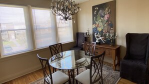 Un comedor con una mesa de vidrio, sillas, una lámpara de araña, un tapete y un cuadro en la pared.