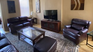 Un salón con sofá, sillón, reposapiés, televisor y ventilador de techo.
