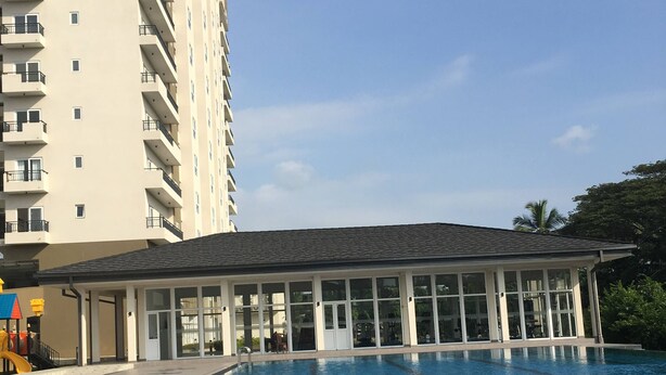 Una piscina con solárium empedrado, un área de descanso cubierta y un edificio residencial alto al fondo.