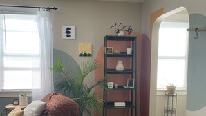 Ein gemütliches Wohnzimmer mit einem braunen Sitzsack, einem hohen schwarzen Bücherregal und einer großen Topfpflanze.