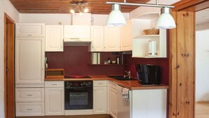 A compact kitchen with white cabinets, a stove, a dishwasher, and a coffee maker. - Holiday apartment  (Todtnau)