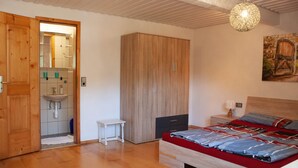 A bedroom with a wooden wardrobe, a bed with a red and blue bedspread, a small white table, and a hanging light fixture. - Holiday apartment  (Todtnau)