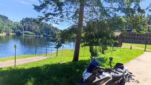 A motorcycle parked on a paved path near a lake, with a building in the background. - Holiday apartment  (Todtnau)