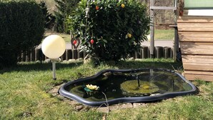 A garden with a pond, a wooden deck, and a house in the background. - Holiday apartment  (Todtnau)