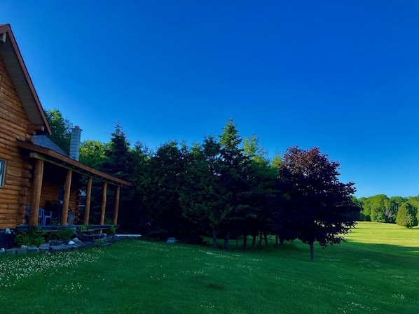 A log cabin with a porch, surrounded by a well-maintained lawn and trees.