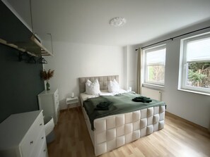 Une chambre à coucher moderne avec un grand lit, une table de chevet, une commode et une fenêtre avec des stores.