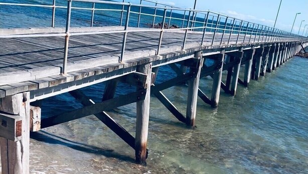 A pier extending into clear shallow waters with a sandy beach at the end. - Stunning beachfront view ,  (North Beach)