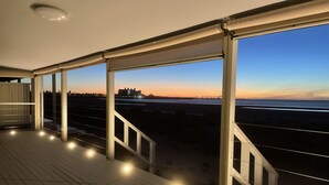 A wooden deck with railings and lights, overlooking a beach and a distant cityscape during twilight. - Stunning beachfront view ,  (North Beach)