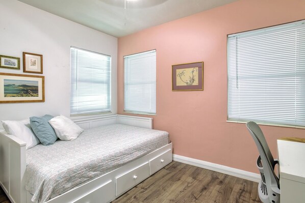 A bedroom with a bed, two windows, a guitar, and framed pictures on the wall.