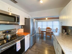 A modern kitchen with stainless steel appliances, a wooden dining table, and a view of the outside through large windows.